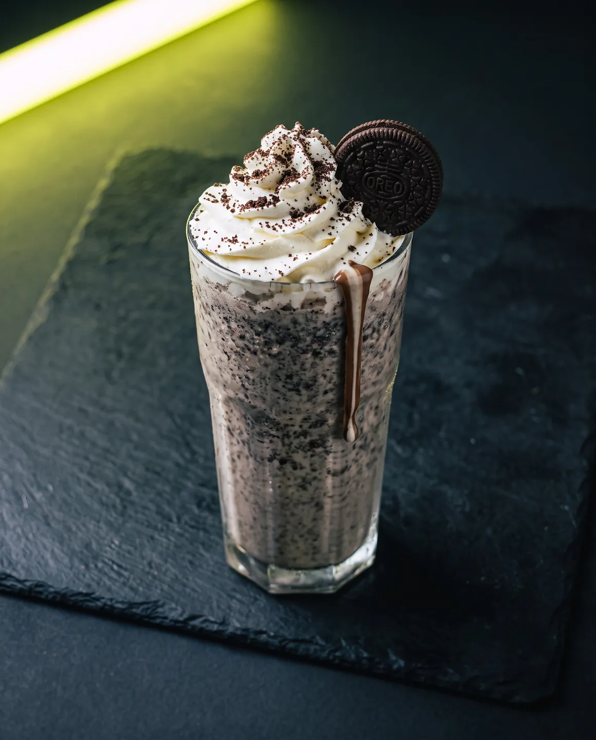 Malteada de Oreo de La Cuadra en vaso alto, con la luz de neón lima recortándole el borde